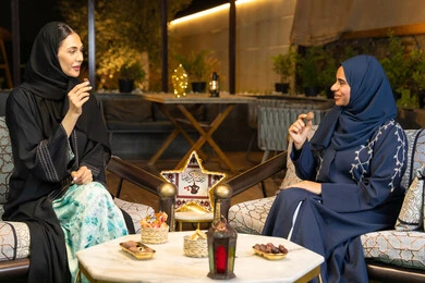 تناول التمر السكري الطازج، منتج وطني محلي اماراتي، حسن الاستقبال في شهر رمضان المبارك، زينة واضاءة رمضانية، امراتان سعوديتان تجلسان بالجلسة الخارجية في احدى شاليهات الامارات، صديقتان عربيتان خليجيتان اماراتيتان ترتديان العباءة تجلسان في الهواء الطلق