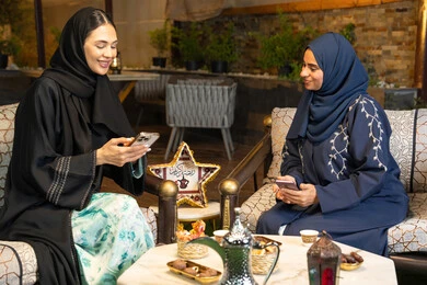 اضواء و زينة رمضانية، استخدام جهاز الهاتف المحمول، امراتان سعوديتان تجلسان بالجلسة الخارجية في احدى شاليهات الامارات، حسن الاستقبال في شهر رمضان المبارك، صديقتان عربيتان خليجيتان اماراتيتان ترتديان العباءة تجلسان في الهواء الطلق