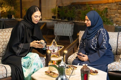 تقاليد وعادات شرب القهوة التقليدية، امراتان سعوديتان تجلسان بالجلسة الخارجية في احدى شاليهات الامارات، حسن الاستقبال في شهر رمضان المبارك، صديقتان عربيتان خليجيتان اماراتيتان ترتديان العباءة تجلسان في الهواء الطلق، منتج وطني محلي اماراتي، زينة واضاءة رمضانية