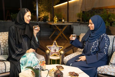عادات وتقاليد شرب القهوة التقليدية، امراتان سعوديتان تجلسان بالجلسة الخارجية في احدى شاليهات الامارات، حسن الاستقبال في شهر رمضان المبارك، صديقتان عربيتان خليجيتان اماراتيتان ترتديان العباءة تجلسان في الهواء الطلق، منتج وطني محلي اماراتي، زينة واضاءة رمضانية
