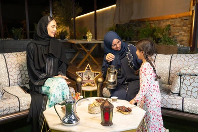 Ramadan decorations and lighting, warm welcome and hospitality during the holy month of Ramadan, an outdoor evening gathering in one of the chalets in the Emirates, an Emirati Gulf Arab woman sitting outdoors with her friend and daughter, two Saudi women exchanging conversations and news with expressions of pleasure