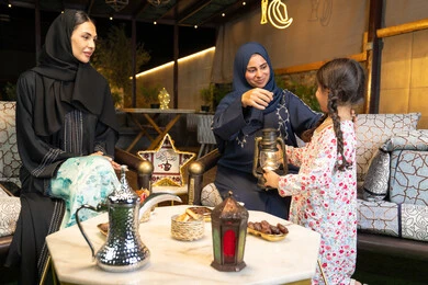 حسن الاستقبال وكرم الضيافة في شهر رمضان المبارك، زينة واضاءة رمضانية، الجلسة الليلة الخارجية في احدى شاليهات الامارات،  امراة عربية خليجية اماراتية تجلس في الهواء الطلق مع صديقتها وابنتها، سيدتان سعوديتان تقومان بتبادل الاحاديث والاخبار بتعابير السرور