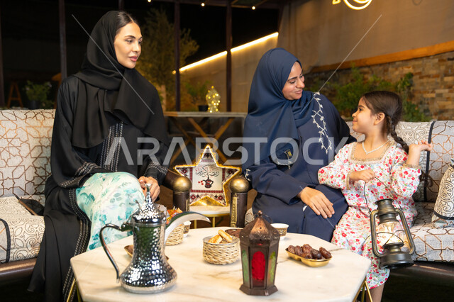 الجلسة الليلة الخارجية في احدى شاليهات الامارات، زينة واضاءة رمضانية، حسن الاستقبال وكرم الضيافة في شهر رمضان المبارك، امراة عربية خليجية اماراتية تجلس في الهواء الطلق مع صديقتها وابنتها، سيدتان سعوديتان تقومان بتبادل الاحاديث والاخبار بتعابير السرور