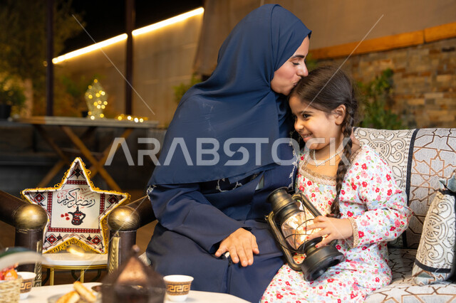 زينة واضاءة شهر رمضان المبارك، الجلسة الليلة الخارجية في احدى شاليهات الامارات،  امراة عربية خليجية اماراتية تجلس في الهواء الطلق، سيدة سعودية تقوم بتقبيل ابنتها، فتاة تحمل بيدها فانوس رمضاني