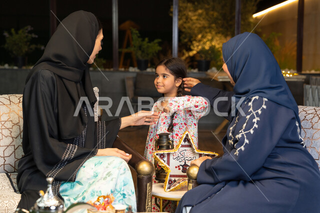 حسن الاستقبال وكرم الضيافة في شهر رمضان المبارك، زينة واضاءة رمضانية، الجلسة الليلة الخارجية في احدى شاليهات الامارات،  امراة عربية خليجية اماراتية تجلس في الهواء الطلق مع صديقتها وابنتها، سيدتان سعوديتان تقومان بتبادل الاحاديث والاخبار بتعابير السرور
