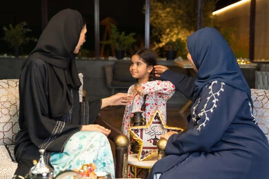 حسن الاستقبال وكرم الضيافة في شهر رمضان المبارك، زينة واضاءة رمضانية، الجلسة الليلة الخارجية في احدى شاليهات الامارات،  امراة عربية خليجية اماراتية تجلس في الهواء الطلق مع صديقتها وابنتها، سيدتان سعوديتان تقومان بتبادل الاحاديث والاخبار بتعابير السرور