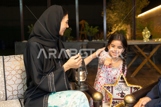 زينة واضاءة رمضانية، حسن الاستقبال وكرم الضيافة في شهر رمضان المبارك، الجلسة الليلة الخارجية في احدى شاليهات الامارات،  امراة عربية خليجية اماراتية تجلس في الهواء الطلق مع صديقتها وابنتها، سيدتان سعوديتان تقومان بتبادل الاحاديث والاخبار بتعابير السرور