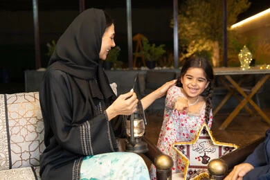 Ramadan decorations and lighting, warm welcome and hospitality during the holy month of Ramadan, an outdoor evening gathering in one of the chalets in the Emirates, an Emirati Gulf Arab woman sitting outdoors with her friend and daughter, two Saudi women exchanging conversations and news with expressions of pleasure