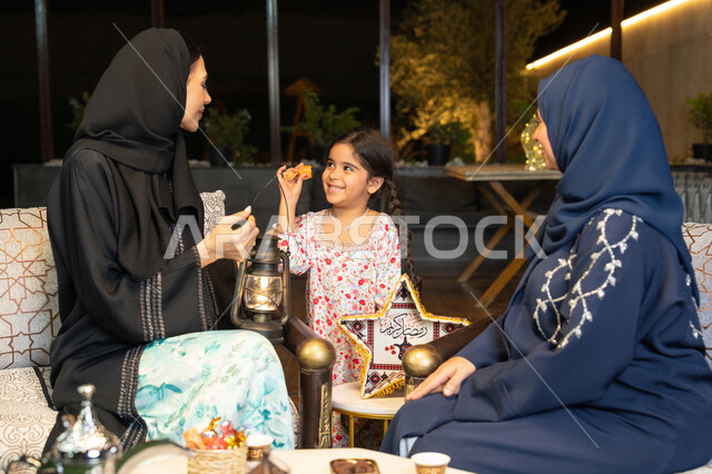الجلسة الليلة الخارجية في احدى شاليهات الامارات، زينة واضاءة رمضانية، حسن الاستقبال وكرم الضيافة في شهر رمضان المبارك، امراة عربية خليجية اماراتية تجلس في الهواء الطلق مع صديقتها وابنتها، سيدتان سعوديتان تقومان بتبادل الاحاديث والاخبار بتعابير السرور