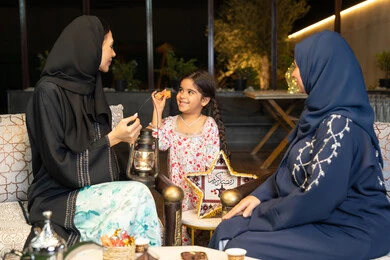 الجلسة الليلة الخارجية في احدى شاليهات الامارات، زينة واضاءة رمضانية، حسن الاستقبال وكرم الضيافة في شهر رمضان المبارك، امراة عربية خليجية اماراتية تجلس في الهواء الطلق مع صديقتها وابنتها، سيدتان سعوديتان تقومان بتبادل الاحاديث والاخبار بتعابير السرور