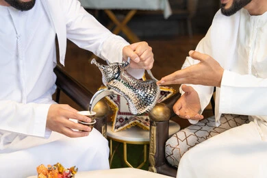 عادات وتقاليد شرب القهوة التقليدية، الجلسة الليلة الخارجية في احدى شاليهات الامارات، حسن الاستقبال والكرم في شهر رمضان المبارك، صديقان عربيان خليجيان اماراتيان يرتديان الكندورة والغترة يجلسان في الهواء الطلق، منتج وطني محلي اماراتي، زينة واضاءة رمضانية