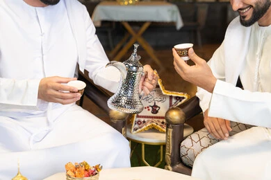 ديكور واضاءة رمضانية، عادات وتقاليد شرب القهوة التقليدية، الجلسة الليلة الخارجية في احدى شاليهات الامارات، حسن الاستقبال والكرم في شهر رمضان المبارك، صديقان عربيان خليجيان اماراتيان يرتديان الكندورة والغترة يجلسان في الهواء الطلق، منتج وطني محلي اماراتي