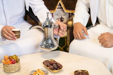 تقاليد وعادات شرب القهوة التقليدية، الجلسة الليلة الخارجية في احدى شاليهات الامارات، حسن الاستقبال والكرم في شهر رمضان المبارك، صديقان عربيان خليجيان اماراتيان يرتديان الكندورة والغترة يجلسان في الهواء الطلق، منتج وطني محلي اماراتي، زينة واضاءة رمضانية