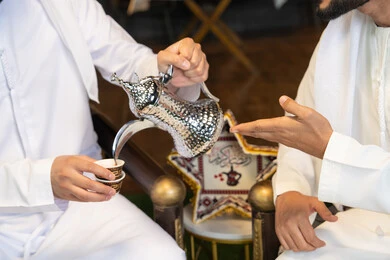 عادات وتقاليد شرب القهوة التقليدية، الجلسة الليلة الخارجية في احدى شاليهات الامارات، حسن الاستقبال والكرم في شهر رمضان المبارك، صديقان عربيان خليجيان اماراتيان يرتديان الكندورة والغترة يجلسان في الهواء الطلق، منتج وطني محلي اماراتي، زينة واضاءة رمضانية