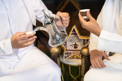 زينة واضاءة رمضانية، عادات وتقاليد شرب القهوة التقليدية، الجلسة الليلة الخارجية في احدى شاليهات الامارات، حسن الاستقبال والكرم في شهر رمضان المبارك، صديقان عربيان خليجيان اماراتيان يرتديان الكندورة والغترة يجلسان في الهواء الطلق، منتج وطني محلي اماراتي