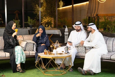 مجموعة من الأصدقاء العرب الخليجيين الاماراتيين يجلسون في الهواء الطلق، تبادل الاحاديث والاخبار بتعابير السرور والسعادة، زينة واضاءة رمضانية، الجلسة الليلة الخارجية في احدى شاليهات الامارات، حسن الاستقبال وكرم الضيافة في شهر رمضان المبارك