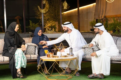 مجموعة من الأصدقاء العرب الخليجيين الاماراتيين يجلسون في الهواء الطلق، تبادل الاحاديث والاخبار بتعابير السرور والسعادة، زينة واضاءة رمضانية، الجلسة الليلة الخارجية في احدى شاليهات الامارات، حسن الاستقبال وكرم الضيافة في شهر رمضان المبارك