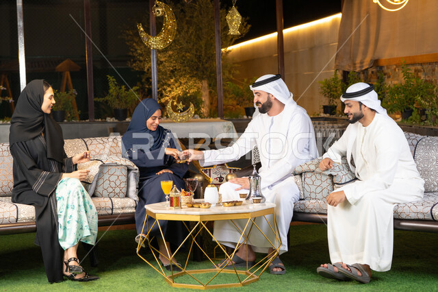 تبادل الاحاديث والاخبار بتعابير السرور والسعادة، حسن الاستقبال وكرم الضيافة في شهر رمضان المبارك، الجلسة الليلة الخارجية في احدى شاليهات الامارات، زينة واضاءة رمضانية، مجموعة من الأصدقاء العرب الخليجيين الاماراتيين يجلسون في الهواء الطلق