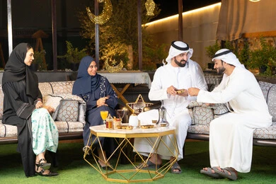 الجلسة الليلة الخارجية في احدى شاليهات الامارات، زينة واضاءة رمضانية، حسن الاستقبال وكرم الضيافة في شهر رمضان المبارك، مجموعة من الأصدقاء العرب الخليجيين الاماراتيين يجلسون في الهواء الطلق، تبادل الاحاديث والاخبار بتعابير السرور والسعادة