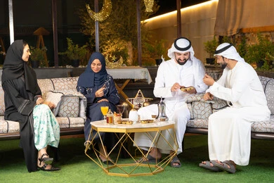 Warm welcome and hospitality during the holy month of Ramadan, an outdoor evening gathering in one of the chalets in the Emirates, Ramadan decorations and lighting, a group of Emirati Gulf Arab friends sitting in the open air, exchanging conversations and news with expressions of pleasure and happiness.