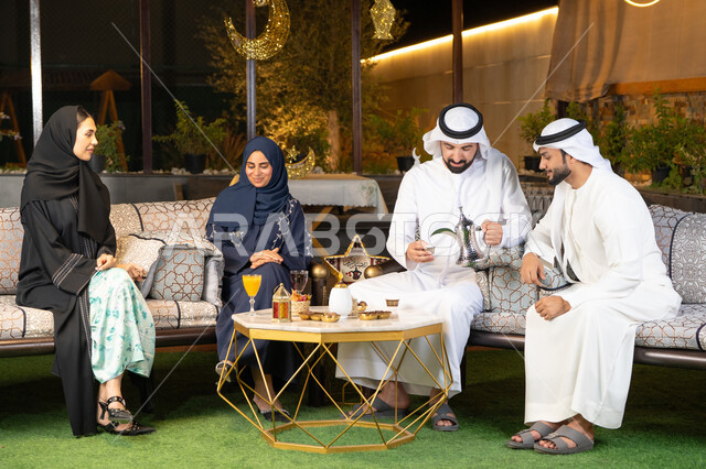 An outdoor evening session in one of the chalets in the Emirates, Ramadan decorations and lighting, warm welcome and hospitality in the holy month of Ramadan, a group of Arab Gulf Emirati friends sitting in the open air, exchanging conversations and news with expressions of pleasure and happiness
