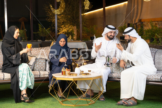 الجلسة الليلة الخارجية في احدى شاليهات الامارات، زينة واضاءة رمضانية، حسن الاستقبال وكرم الضيافة في شهر رمضان المبارك، مجموعة من الأصدقاء العرب الخليجيين الاماراتيين يجلسون في الهواء الطلق، تبادل الاحاديث والاخبار بتعابير السرور والسعادة