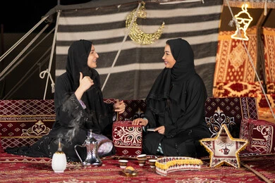 التحدث والتسامر في السوالف السعيده، سيدتان عربيتان خليجيتان تقومان بالتحدث في موضوع ما, استخدام احدث التقنيات الحديثه, امراتين سعوديتان ترتديان العباءه والحجاب تجلسان في الخيمه ليلا، اصول المجلس الشعبي