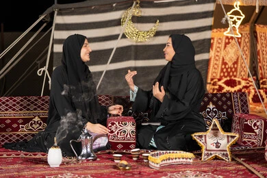 التحدث والتسامر في السوالف السعيده، سيدتان عربيتان خليجيتان تقومان بالتحدث في موضوع ما, استخدام احدث التقنيات الحديثه, امراتين سعوديتان ترتديان العباءه والحجاب تجلسان في الخيمه ليلا، اصول المجلس الشعبي