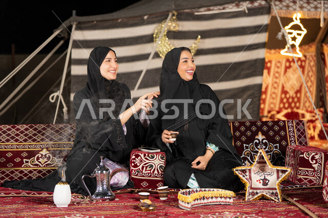 ايماءه الاشاره الي شئ ما، التحدث والتسامر في السوالف السعيده، سيدتان عربيتان خليجيتان تقومان بالنظرالي شئ ما, امراتين سعوديتان ترتديان العباءه والحجاب تجلسان في الخيمه ليلا، اصول المجلس الشعبي، امرأه اماراتيه تشير باصبع السبابه