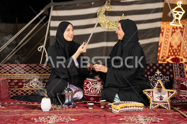 تناول حبه التمر لكسر الصيام, حسن الاستقبال وكرم الضيافه، سيده امارتيه تقوم بتقديم التمر لصديقتها، امراءه سعوديه تحمل بيدها طبق مليئ بالرطب، خيمه مليئه بزينه وديكورات رمضانيه