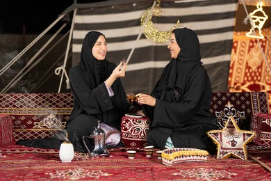 تناول حبه التمر لكسر الصيام, حسن الاستقبال وكرم الضيافه، سيده امارتيه تقوم بتقديم التمر لصديقتها، امراءه سعوديه تحمل بيدها طبق مليئ بالرطب، خيمه مليئه بزينه وديكورات رمضانيه