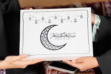 صورة مقربه  ليد امراتين سعوديتان تمسكان علبة هدايا عليها مخطوطة مبارك عليكم الشهر مع هلال وفوانيس رمضان باللون الاسود،  التهنئه  وتقديم الهديه في شهر رمضان المبارك ، مناسبه دينيه إسلاميه، سيده عربيه خليجيه اماراتيه تقدم هديه لصديقتها