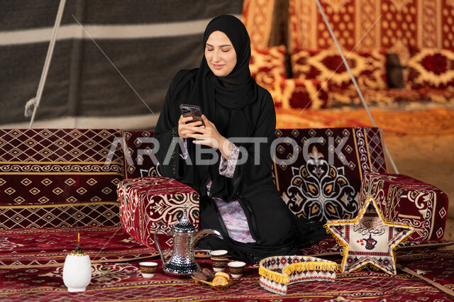 إيماءات السرور والسعادة، الدردشه مع الأهل والأصدقاء، استخدام التكنولوجيا والتقنيات الحديثة المتطورة، امرأة عربية سعودية خليجية محجبة تنظرالي الهاتف، سيده اماراتيه تقوم بالرد على الرسائل النصيه، استخدام التقنيات والاجهزه الحديثه