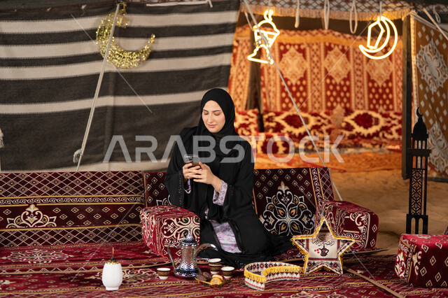إيماءات السرور والسعادة، الدردشه مع الأهل والأصدقاء، استخدام التكنولوجيا والتقنيات الحديثة المتطورة، امرأة عربية سعودية خليجية محجبة تنظرالي الهاتف، سيده اماراتيه تقوم بالرد على الرسائل النصيه، استخدام التقنيات والاجهزه الحديثه