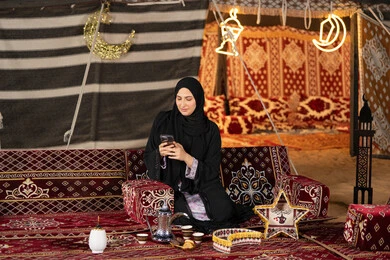 إيماءات السرور والسعادة، الدردشه مع الأهل والأصدقاء، استخدام التكنولوجيا والتقنيات الحديثة المتطورة، امرأة عربية سعودية خليجية محجبة تنظرالي الهاتف، سيده اماراتيه تقوم بالرد على الرسائل النصيه، استخدام التقنيات والاجهزه الحديثه