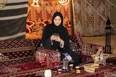 إيماءات السرور والسعادة، الدردشه مع الأهل والأصدقاء، استخدام التكنولوجيا والتقنيات الحديثة المتطورة، امرأة عربية سعودية خليجية محجبة تنظرالي الهاتف، سيده اماراتيه تقوم بالرد على الرسائل النصيه، استخدام التقنيات والاجهزه الحديثه