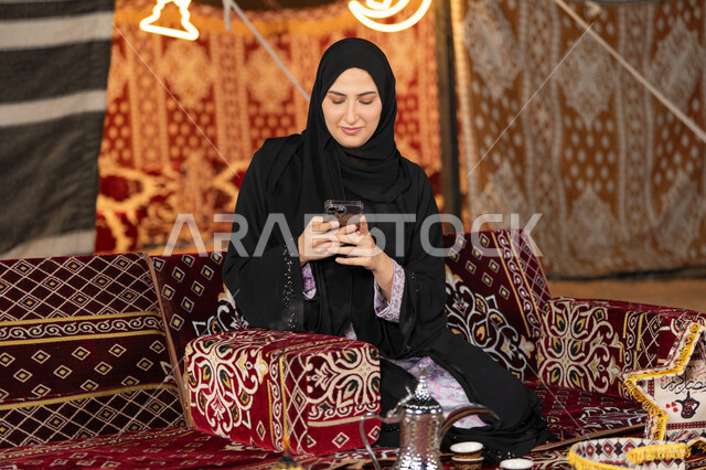 إيماءات السرور والسعادة، الدردشه مع الأهل والأصدقاء، استخدام التكنولوجيا والتقنيات الحديثة المتطورة، امرأة عربية سعودية خليجية محجبة تنظرالي الهاتف، سيده اماراتيه تقوم بالرد على الرسائل النصيه، استخدام التقنيات والاجهزه الحديثه