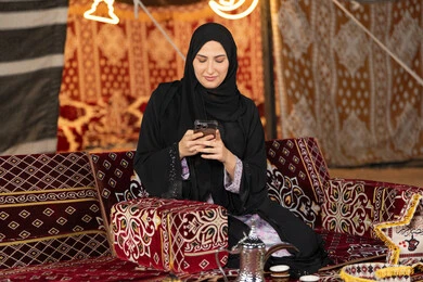 إيماءات السرور والسعادة، الدردشه مع الأهل والأصدقاء، استخدام التكنولوجيا والتقنيات الحديثة المتطورة، امرأة عربية سعودية خليجية محجبة تنظرالي الهاتف، سيده اماراتيه تقوم بالرد على الرسائل النصيه، استخدام التقنيات والاجهزه الحديثه