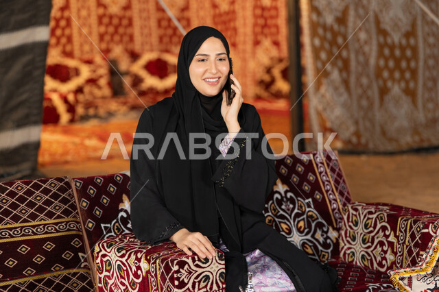 اجراء مكالمه هاتفيه للاطمئنان علي الاصدقاء والاهل، استخدام احدث الاجهزه والتقنيات، التواصل عن بعد، سيده اماراتيه تجري مكالمه هاتفيه مع شخص ما، سيده سعوديه تجلس في خيمه شعبيه ليلا تستخدم الهاتف المحمول، اصول المجلس الشعبي
