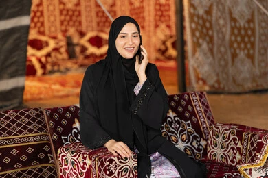 اجراء مكالمه هاتفيه للاطمئنان علي الاصدقاء والاهل، استخدام احدث الاجهزه والتقنيات، التواصل عن بعد، سيده اماراتيه تجري مكالمه هاتفيه مع شخص ما، سيده سعوديه تجلس في خيمه شعبيه ليلا تستخدم الهاتف المحمول، اصول المجلس الشعبي