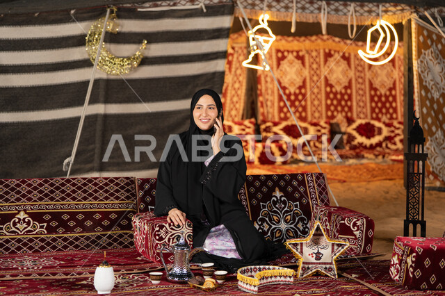 اجراء مكالمه هاتفيه للاطمئنان علي الاصدقاء والاهل، استخدام احدث الاجهزه والتقنيات، التواصل عن بعد، سيده اماراتيه تجري مكالمه هاتفيه مع شخص ما، سيده سعوديه تجلس في خيمه شعبيه ليلا تستخدم الهاتف المحمول، اصول المجلس الشعبي