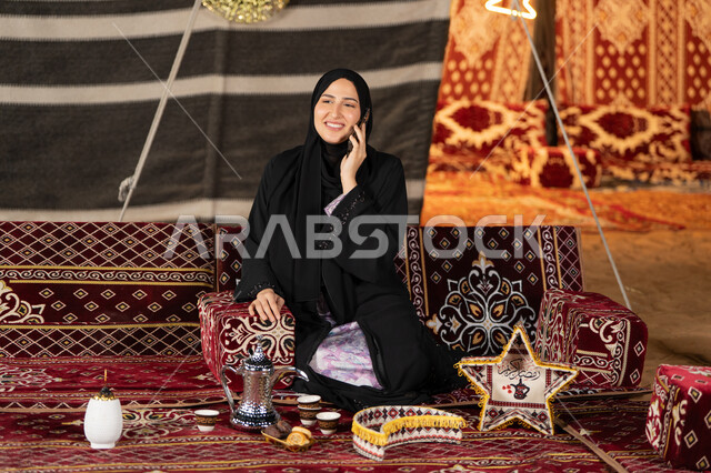 اجراء مكالمه هاتفيه للاطمئنان علي الاصدقاء والاهل، استخدام احدث الاجهزه والتقنيات، التواصل عن بعد، سيده اماراتيه تجري مكالمه هاتفيه مع شخص ما، سيده سعوديه تجلس في خيمه شعبيه ليلا تستخدم الهاتف المحمول، اصول المجلس الشعبي