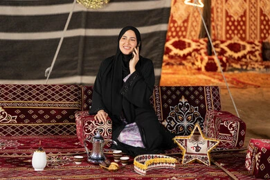 Making a phone call to check on friends and family, using the latest devices and technologies, remote communication, an Emirati woman making a phone call with someone, a Saudi woman sitting in a popular tent at night using a mobile phone, the origins of the popular council