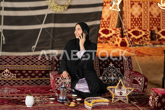 اجراء مكالمه هاتفيه للاطمئنان علي الاصدقاء والاهل، استخدام احدث الاجهزه والتقنيات، التواصل عن بعد، سيده اماراتيه تجري مكالمه هاتفيه مع شخص ما، سيده سعوديه تجلس في خيمه شعبيه ليلا تستخدم الهاتف المحمول، اصول المجلس الشعبي