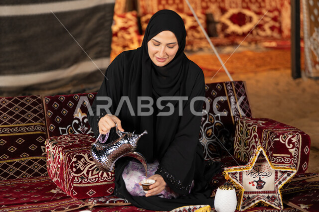 قيم وعادات الضيافه العربيه، حسن الاستقبال وكرم الضيافه،  سيده اماراتيه ترتدي العباءه السوداء تقوم بصب القهوه، امرأه عربيه خليجيه سعوديه مبتسمه تحمل الدله النحاسيه وكوب القهوه, المجلس الشعبي التقليدي