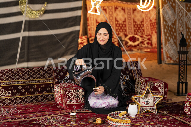 قيم وعادات الضيافه العربيه، حسن الاستقبال وكرم الضيافه،  سيده اماراتيه ترتدي العباءه السوداء تقوم بصب القهوه، امرأه عربيه خليجيه سعوديه مبتسمه تحمل الدله النحاسيه وكوب القهوه, المجلس الشعبي التقليدي