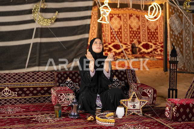الاجتهاد في الطاعات والأدعية، الخشوع والتضرع والطلب من الله، العبادة والتقرب الى الله، إمرأة عربية خليجية سعودية ترتدي الحجاب والعباءة التقليدية ترفع يديها وتنظر الي السماء، سيده اماراتيه تتذلل في طلب الدعاء