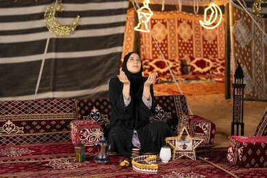 الاجتهاد في الطاعات والأدعية، الخشوع والتضرع والطلب من الله، العبادة والتقرب الى الله، إمرأة عربية خليجية سعودية ترتدي الحجاب والعباءة التقليدية ترفع يديها وتنظر الي السماء، سيده اماراتيه تتذلل في طلب الدعاء