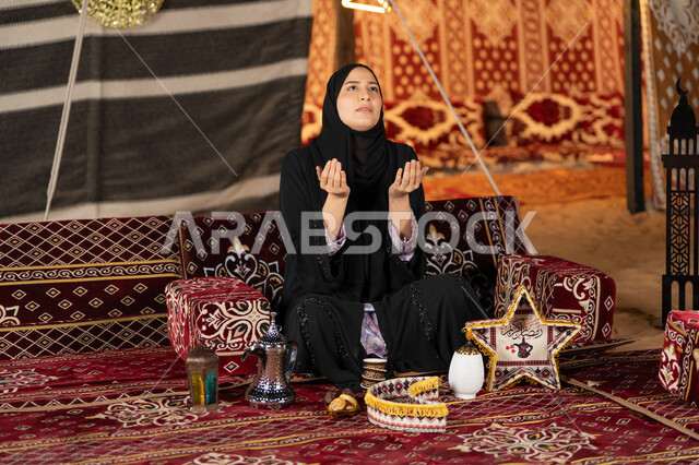 الاجتهاد في الطاعات والأدعية، الخشوع والتضرع والطلب من الله، العبادة والتقرب الى الله، إمرأة عربية خليجية سعودية ترتدي الحجاب والعباءة التقليدية ترفع يديها وتنظر الي السماء، سيده اماراتيه تتذلل في طلب الدعاء
