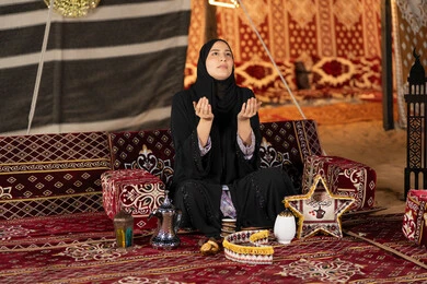 الاجتهاد في الطاعات والأدعية، الخشوع والتضرع والطلب من الله، العبادة والتقرب الى الله، إمرأة عربية خليجية سعودية ترتدي الحجاب والعباءة التقليدية ترفع يديها وتنظر الي السماء، سيده اماراتيه تتذلل في طلب الدعاء